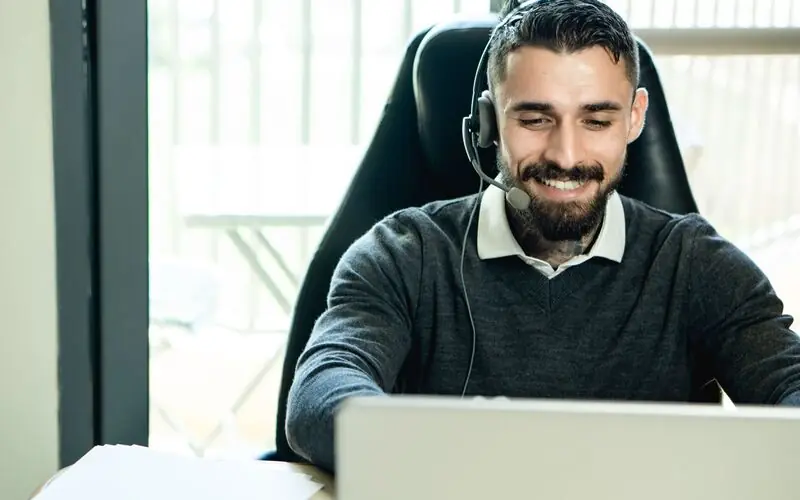 Support agent wearing a headset, smiling while helping a customer on his laptop